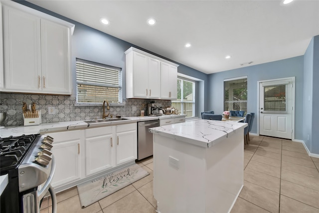 kitchen featuring appliances with stainless steel finishes, light stone counters, white cabinets, backsplash, and a center island