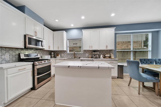 kitchen with white cabinets, light tile patterned flooring, sink, a kitchen island, and appliances with stainless steel finishes