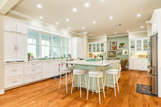 kitchen featuring white cabinets, light stone countertops, a kitchen island with sink, a breakfast bar area, and light wood-type flooring