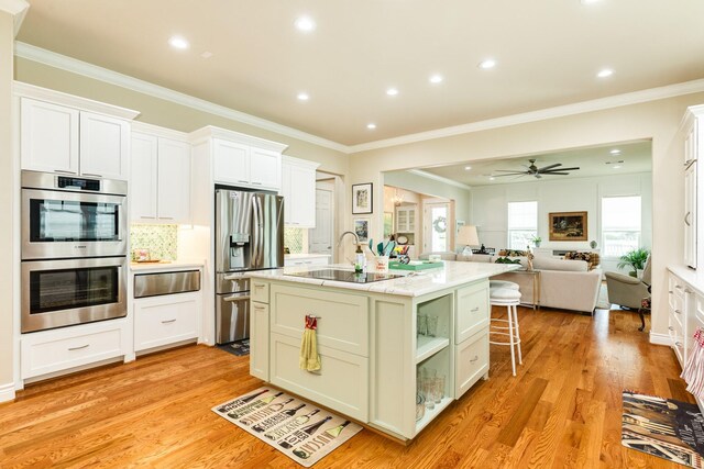 kitchen featuring light hardwood / wood-style floors, an island with sink, white cabinetry, appliances with stainless steel finishes, and ceiling fan