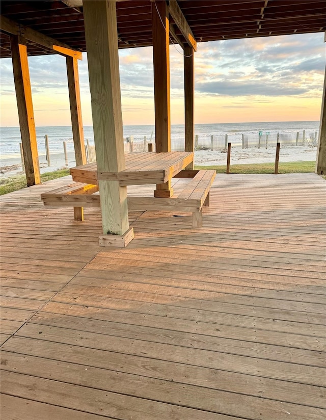 deck at dusk featuring a view of the beach and a water view