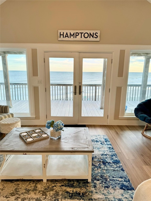 living room with light hardwood / wood-style flooring, a water view, vaulted ceiling, and french doors