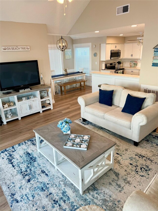 living room featuring ceiling fan with notable chandelier, high vaulted ceiling, and hardwood / wood-style floors