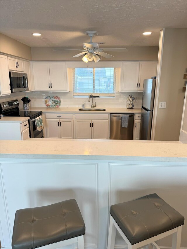 kitchen with appliances with stainless steel finishes, sink, white cabinetry, and a breakfast bar