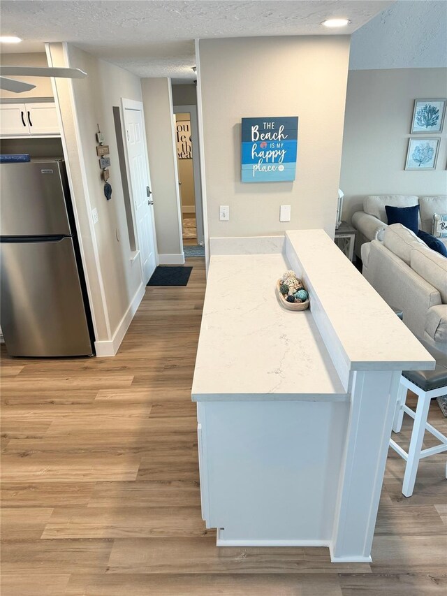 kitchen with white cabinets, a breakfast bar area, light wood-type flooring, and stainless steel fridge