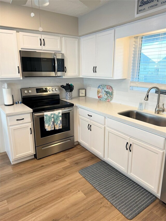 kitchen featuring white cabinetry, tasteful backsplash, stainless steel appliances, light wood-type flooring, and sink