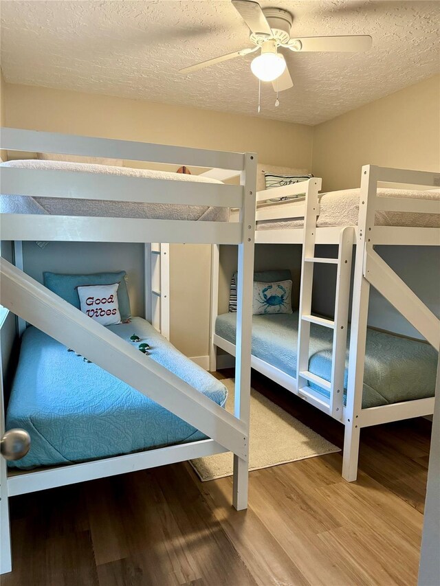 bedroom with a textured ceiling, wood-type flooring, and ceiling fan