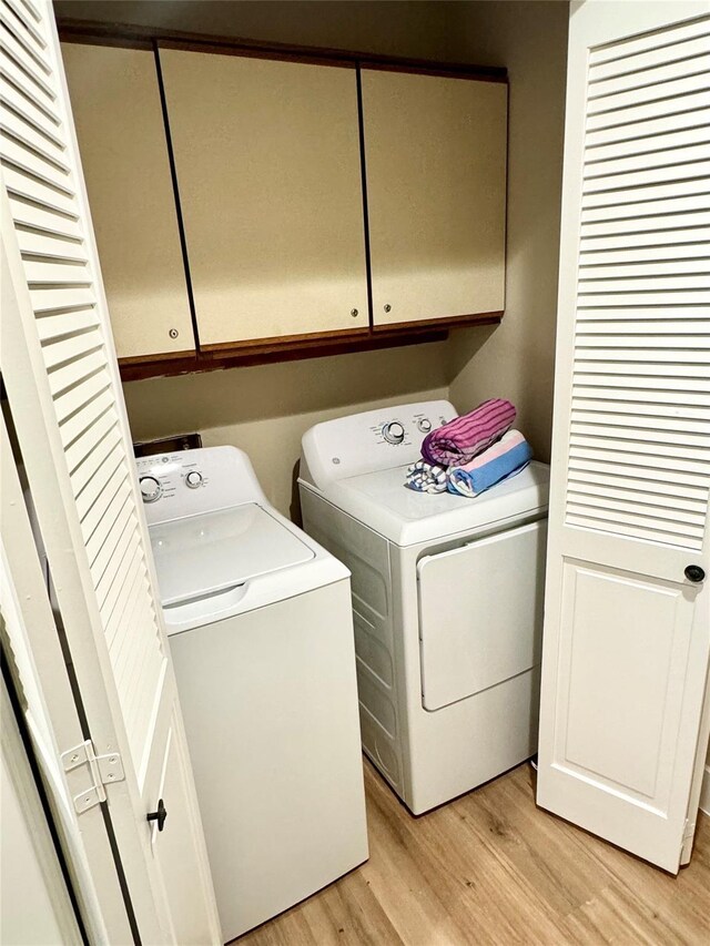 clothes washing area featuring light wood-type flooring, washing machine and dryer, and cabinets