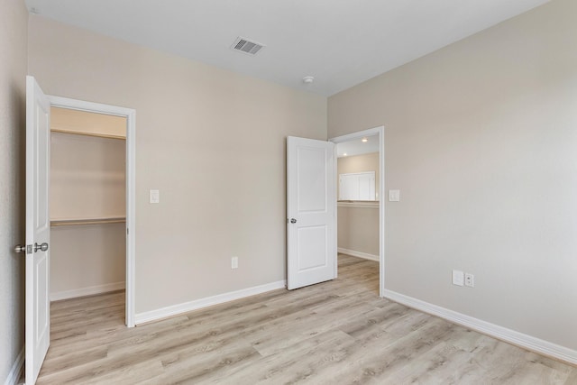 unfurnished bedroom featuring a spacious closet, a closet, and light wood-type flooring