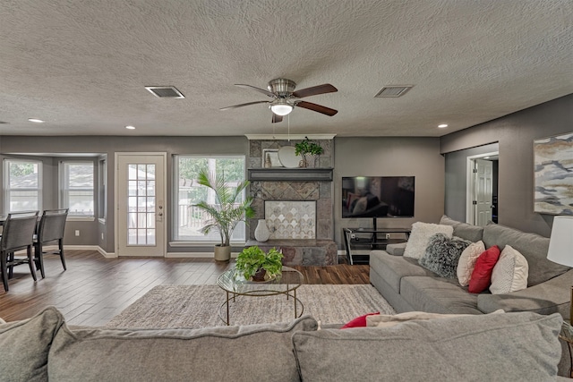 living room with ceiling fan, a stone fireplace, hardwood / wood-style flooring, and a textured ceiling