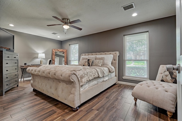 bedroom with ceiling fan, a textured ceiling, dark wood-type flooring, and multiple windows