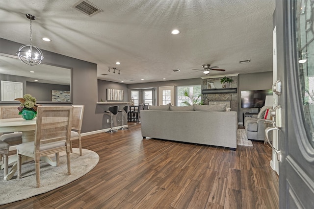 living room with a textured ceiling, ceiling fan with notable chandelier, and dark wood-type flooring