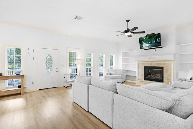 living room featuring ceiling fan, a tiled fireplace, crown molding, and light hardwood / wood-style flooring