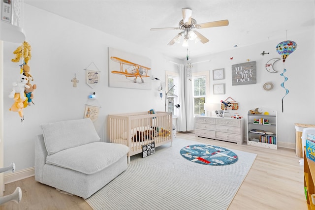 bedroom with ceiling fan, wood-type flooring, and a nursery area