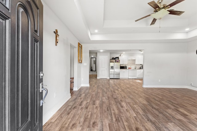 unfurnished living room featuring wood-type flooring, a tray ceiling, and ceiling fan