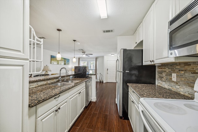 kitchen with dark stone counters, pendant lighting, white cabinetry, appliances with stainless steel finishes, and dark hardwood / wood-style flooring