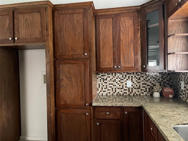 kitchen with backsplash, light stone countertops, and glass insert cabinets