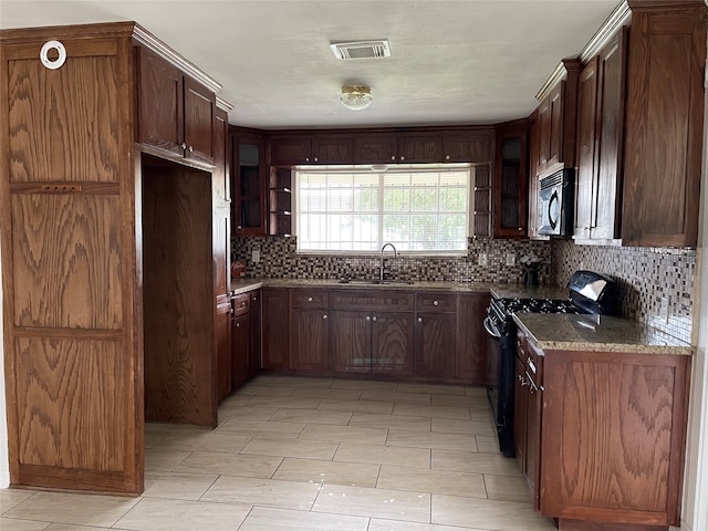 kitchen featuring light stone counters, dark brown cabinetry, sink, tasteful backsplash, and black gas range oven