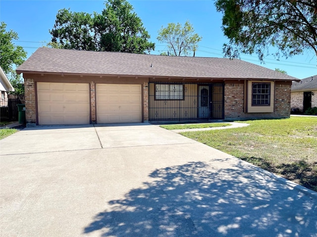single story home featuring a shingled roof, an attached garage, brick siding, a front yard, and concrete driveway