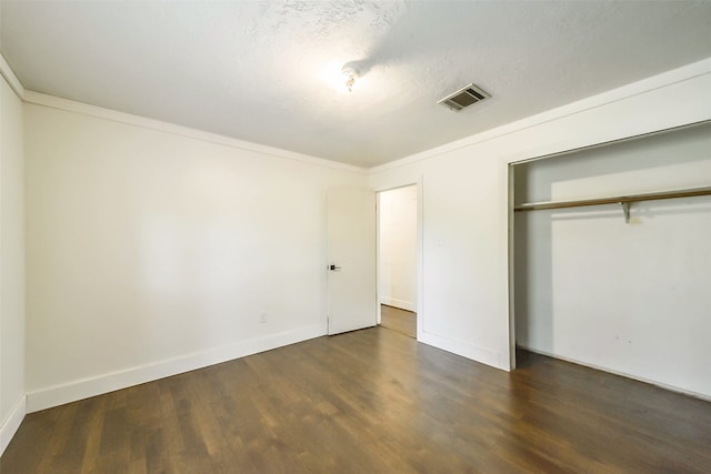 unfurnished bedroom featuring a textured ceiling, a closet, dark hardwood / wood-style floors, and ornamental molding