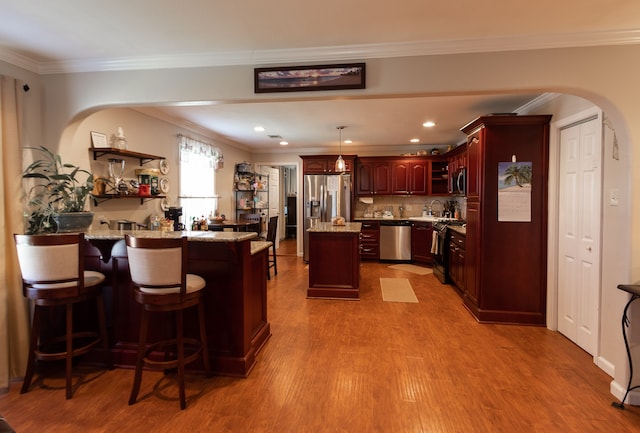 kitchen with ornamental molding, kitchen peninsula, appliances with stainless steel finishes, a breakfast bar area, and hardwood / wood-style floors