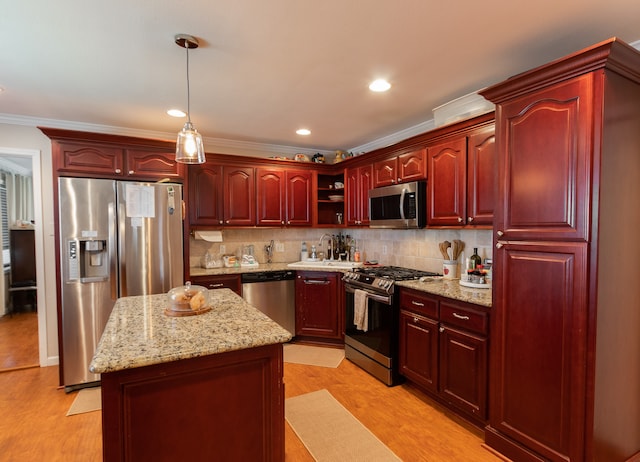 kitchen with appliances with stainless steel finishes, hanging light fixtures, light hardwood / wood-style floors, a kitchen island, and ornamental molding