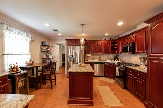 kitchen featuring appliances with stainless steel finishes, pendant lighting, crown molding, a center island, and light hardwood / wood-style flooring