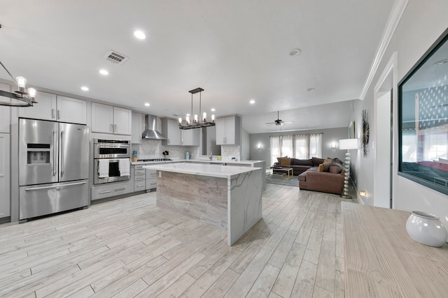 kitchen with wall chimney range hood, light hardwood / wood-style flooring, stainless steel appliances, light stone countertops, and pendant lighting