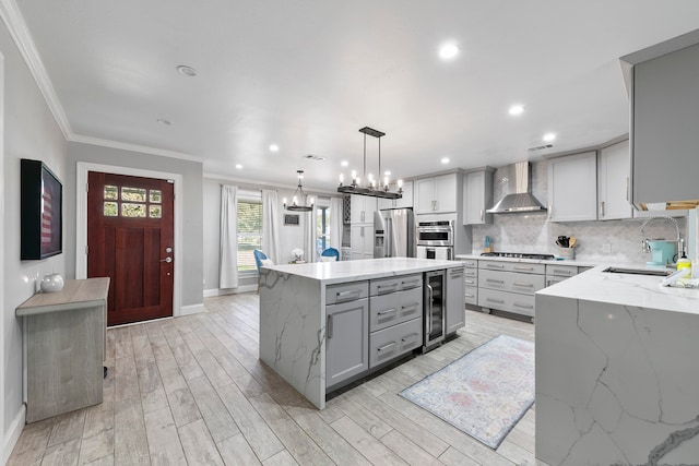 kitchen featuring wall chimney exhaust hood, hanging light fixtures, stainless steel appliances, a center island, and beverage cooler