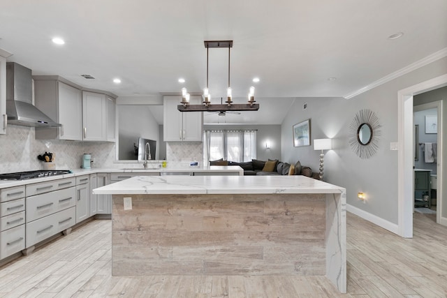 kitchen featuring a spacious island, wall chimney exhaust hood, pendant lighting, and light hardwood / wood-style floors