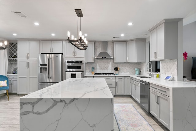 kitchen with light stone counters, appliances with stainless steel finishes, pendant lighting, wall chimney exhaust hood, and sink