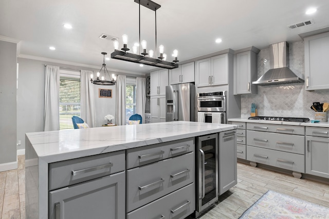 kitchen featuring gray cabinetry, wall chimney range hood, appliances with stainless steel finishes, a kitchen island, and wine cooler