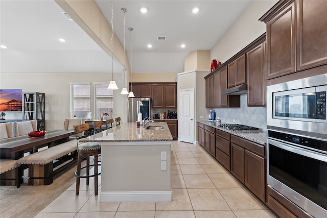 kitchen featuring light stone counters, an island with sink, light tile patterned floors, sink, and stainless steel appliances