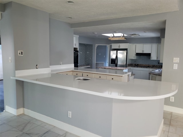 kitchen with stainless steel fridge, kitchen peninsula, a textured ceiling, oven, and white cabinetry