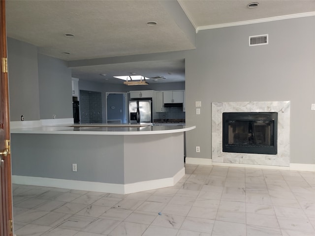 kitchen with white cabinetry, kitchen peninsula, a high end fireplace, crown molding, and stainless steel refrigerator with ice dispenser