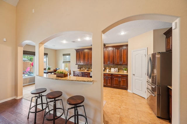 kitchen featuring backsplash, stainless steel refrigerator, a kitchen breakfast bar, light stone countertops, and light hardwood / wood-style floors