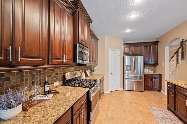 kitchen with decorative backsplash, a textured ceiling, appliances with stainless steel finishes, and light tile patterned floors