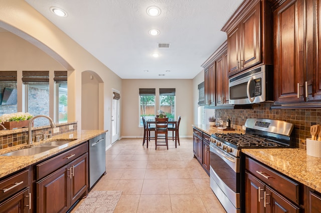 kitchen with light stone counters, light tile patterned flooring, sink, stainless steel appliances, and decorative backsplash