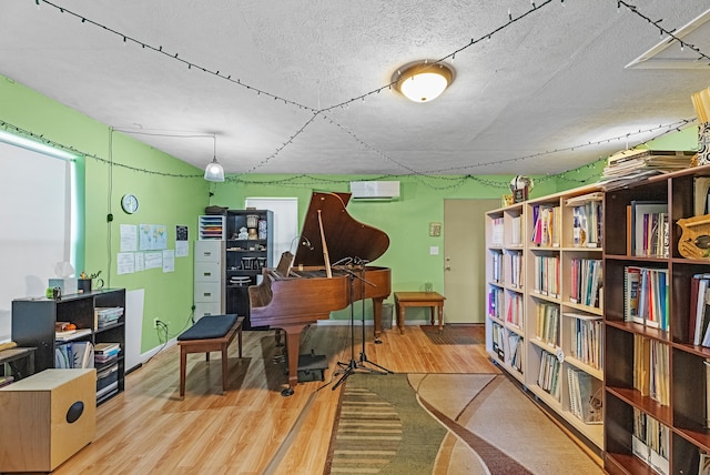 misc room featuring light wood-type flooring, a textured ceiling, and a wall mounted AC