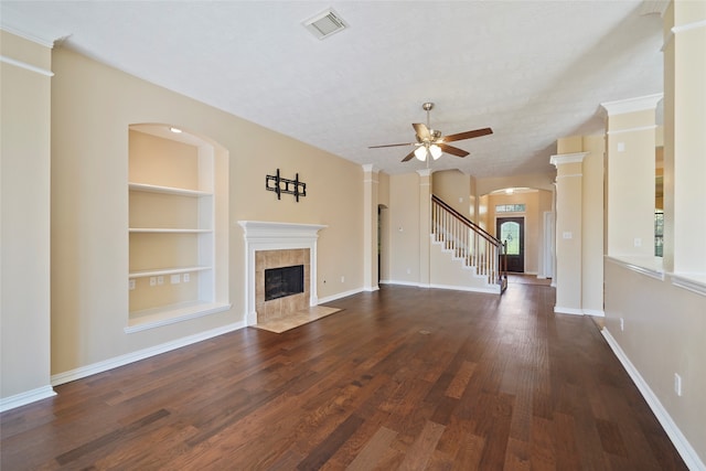 unfurnished living room featuring a textured ceiling, dark hardwood / wood-style floors, built in shelves, a tiled fireplace, and ceiling fan