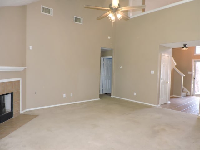 unfurnished living room with a tile fireplace, a high ceiling, ceiling fan, and light carpet