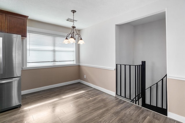 interior space with hanging light fixtures, a textured ceiling, a chandelier, stainless steel refrigerator, and dark hardwood / wood-style floors