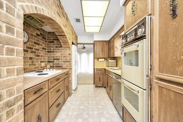 kitchen featuring sink, white appliances, ceiling fan, and brick wall