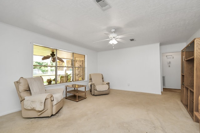 living area featuring ceiling fan, light colored carpet, and a textured ceiling