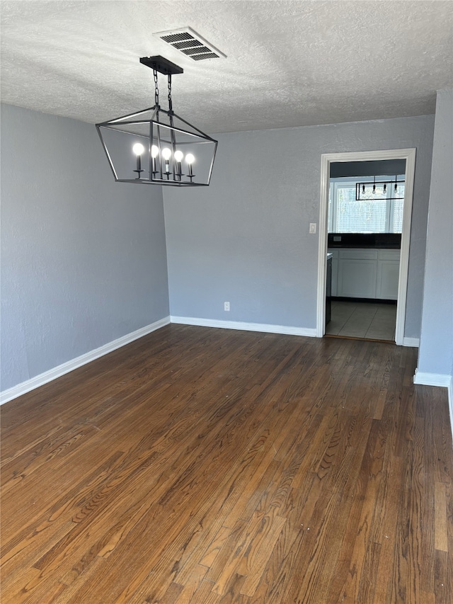 unfurnished room with a notable chandelier, a textured ceiling, and dark wood-type flooring