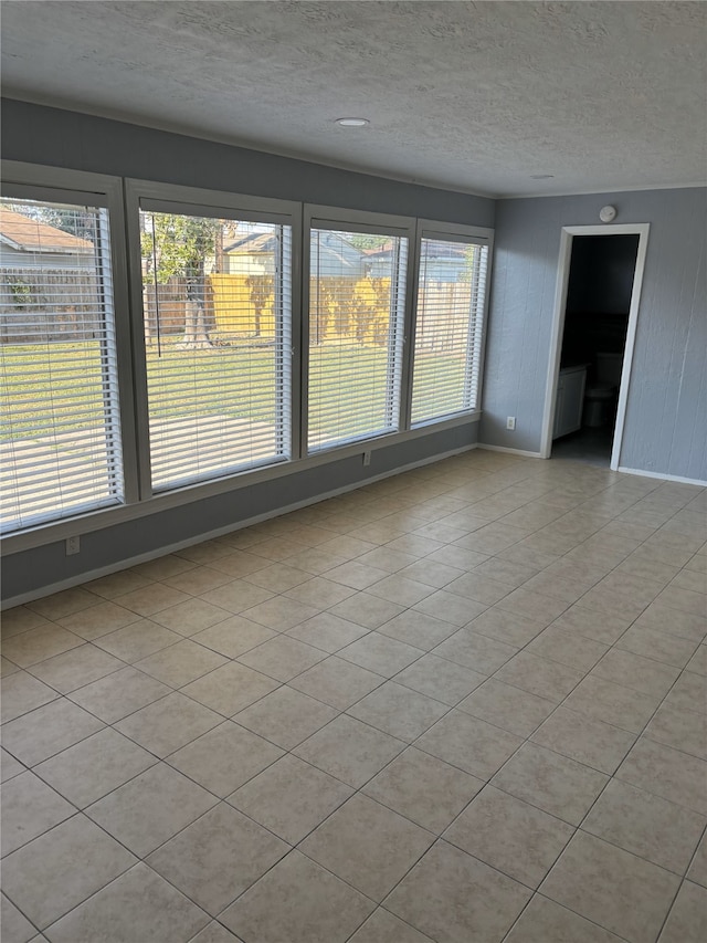 spare room featuring wood walls, a textured ceiling, plenty of natural light, and light tile patterned flooring