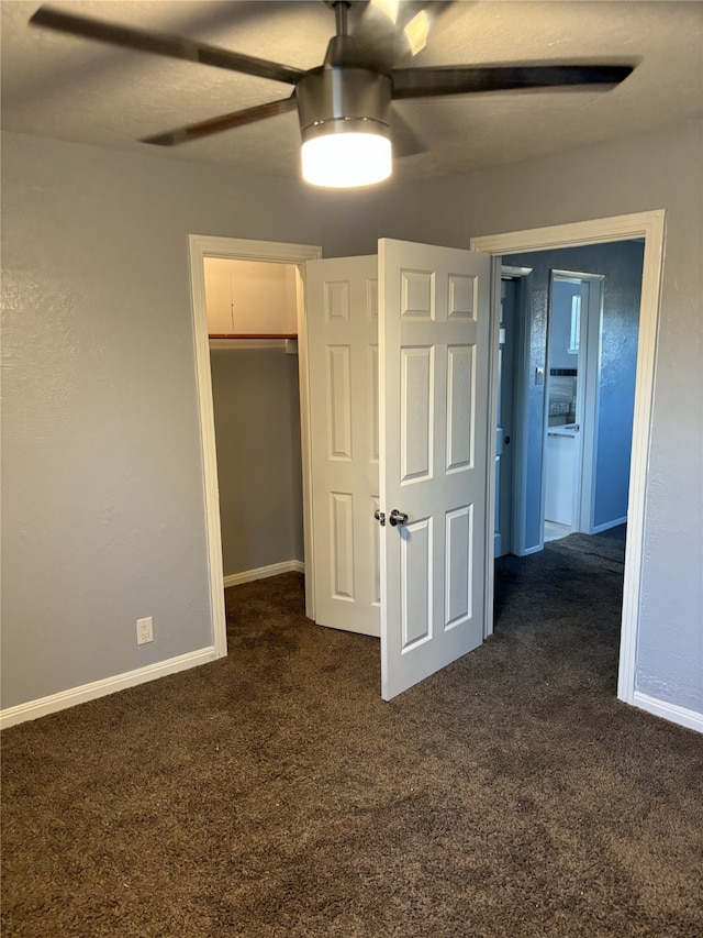 unfurnished bedroom featuring a closet, dark colored carpet, ceiling fan, and a walk in closet