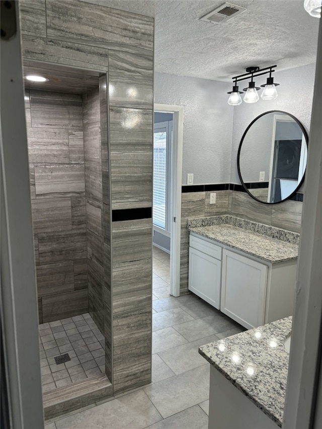 bathroom with a shower, tile walls, vanity, a textured ceiling, and tile patterned floors