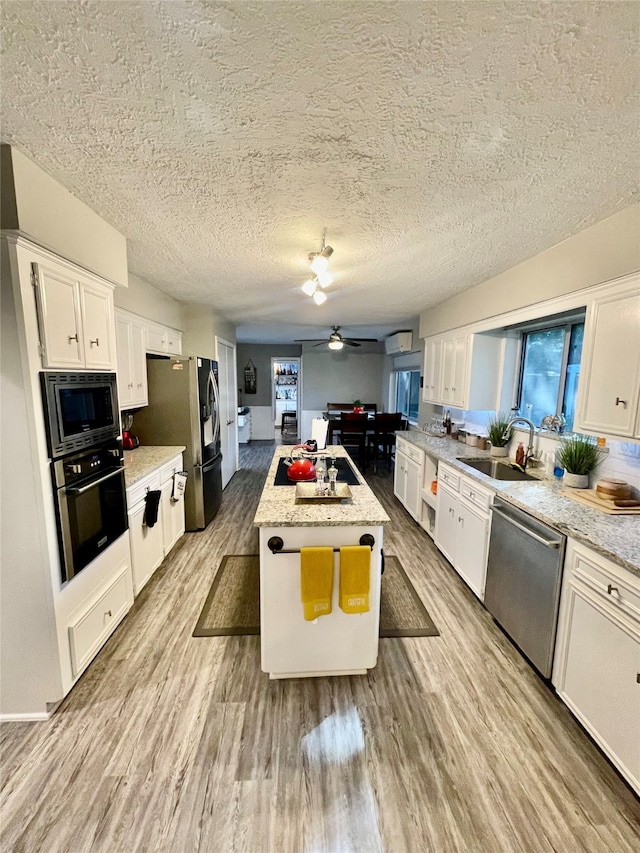 kitchen with ceiling fan, white cabinets, a kitchen island, stainless steel appliances, and light hardwood / wood-style floors