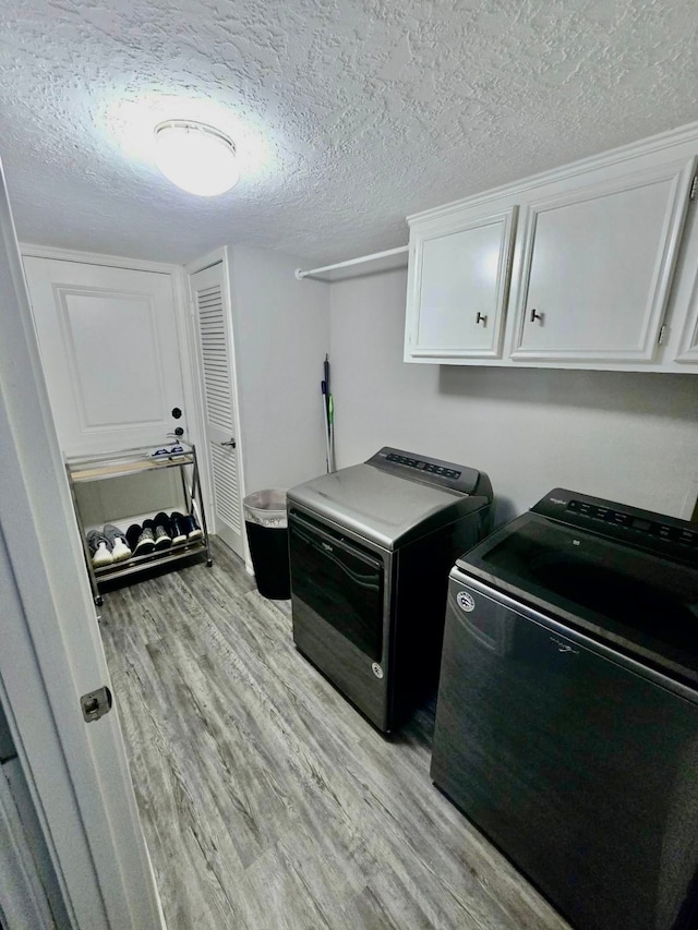 laundry area featuring a textured ceiling, washing machine and dryer, light hardwood / wood-style floors, and cabinets